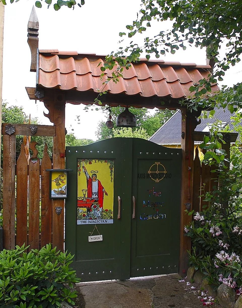 Den grønne port under et tegltag, med tarotkortet Magikeren på lågen og blomster foran