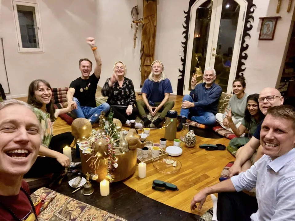 Integrationsaften efter ayahuasca-retreatet: deltagerne sidder i en rundkreds på gulvet i Rundsalen om tændte stearinlys, kopper og en kande te; flere griner og vinker til kameraet