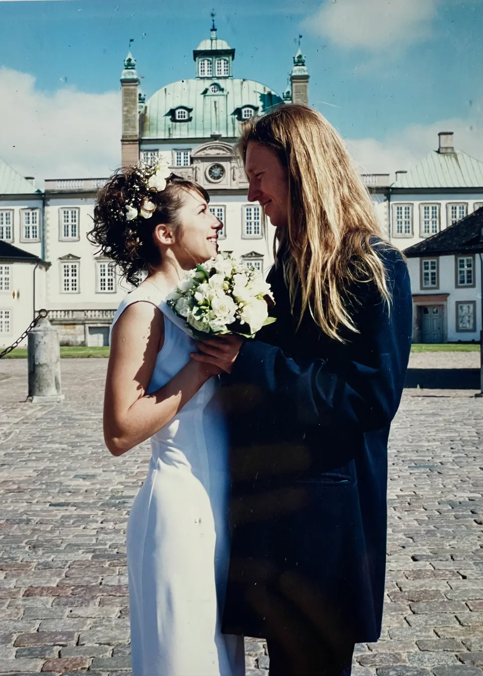 Jacob og Ecaterina Moth på deres bryllupsdag i 2000 foran Fredensborg Slot. Hun i hvid kjole med en buket hvide roser, han med langt lyst hår. De ser hinanden i øjnene.