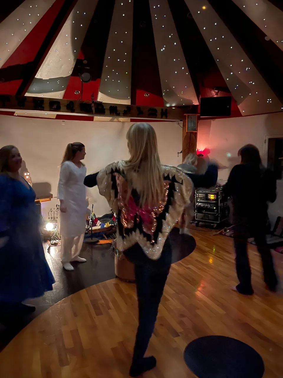 Kvinder danser på trægulvet i Rundsalen, hvor kvindernes ayahuasca-retreats foregår; en af dem har et sommerfuglesjal om skuldrene