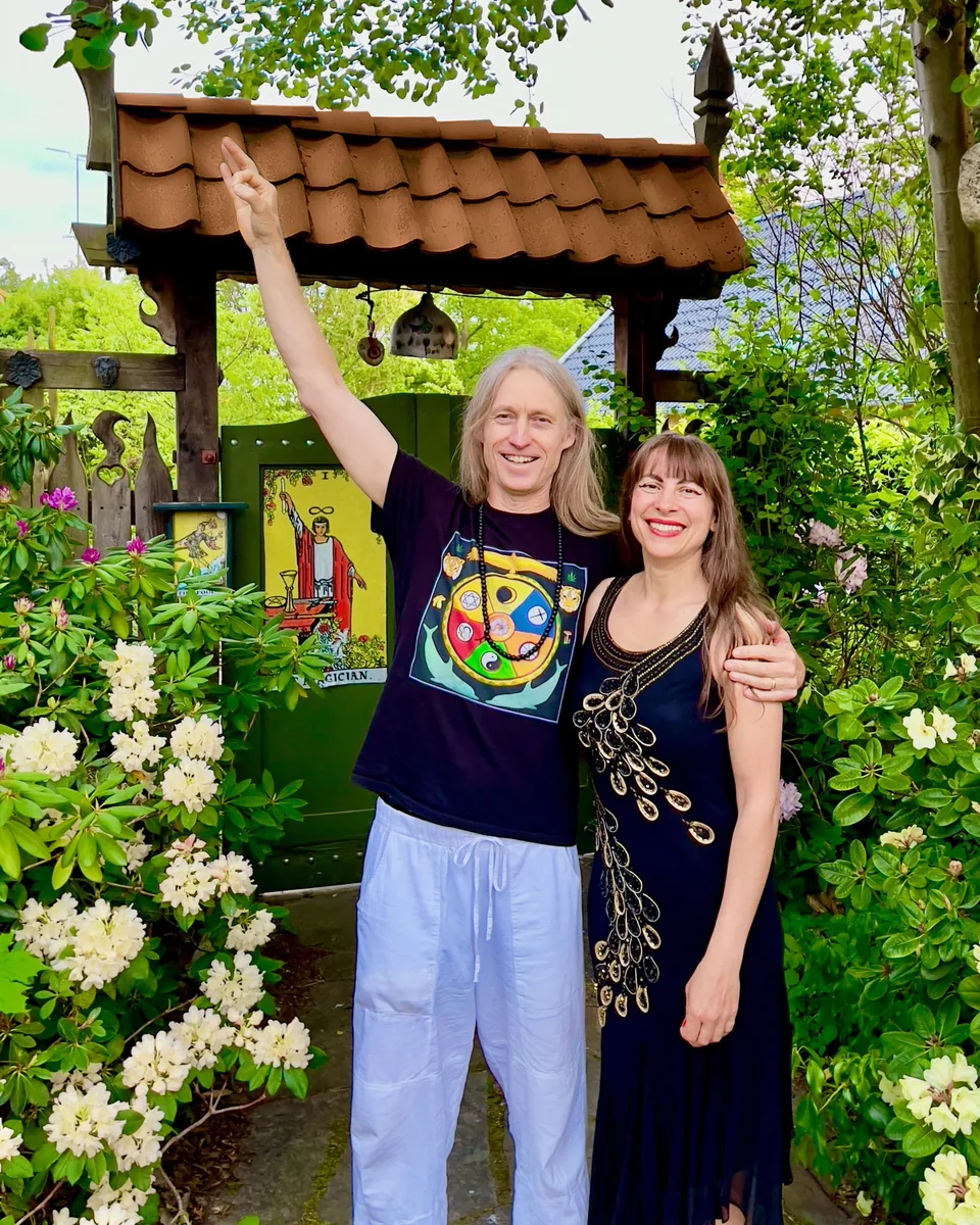 Jacob and Ecaterina Moth standing arm in arm in front of the garden's green gate with the tarot card The Fool, Jacob pointing at the sky