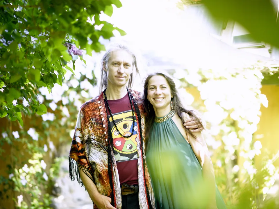 Jacob og Ecaterina Moth står tæt sammen i haven i modlys, mellem grønne blade og hvide blomster