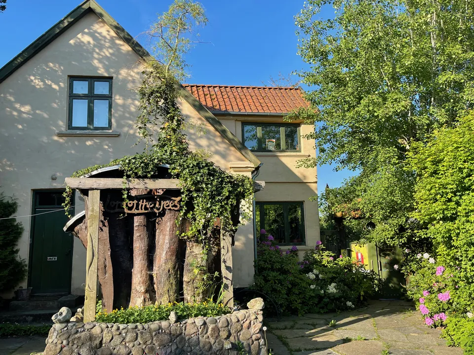 Kronprinsessevej 11 en sommerdag: huset, den høje træstub Træernes Herre og den grønne port mellem blomstrende buske