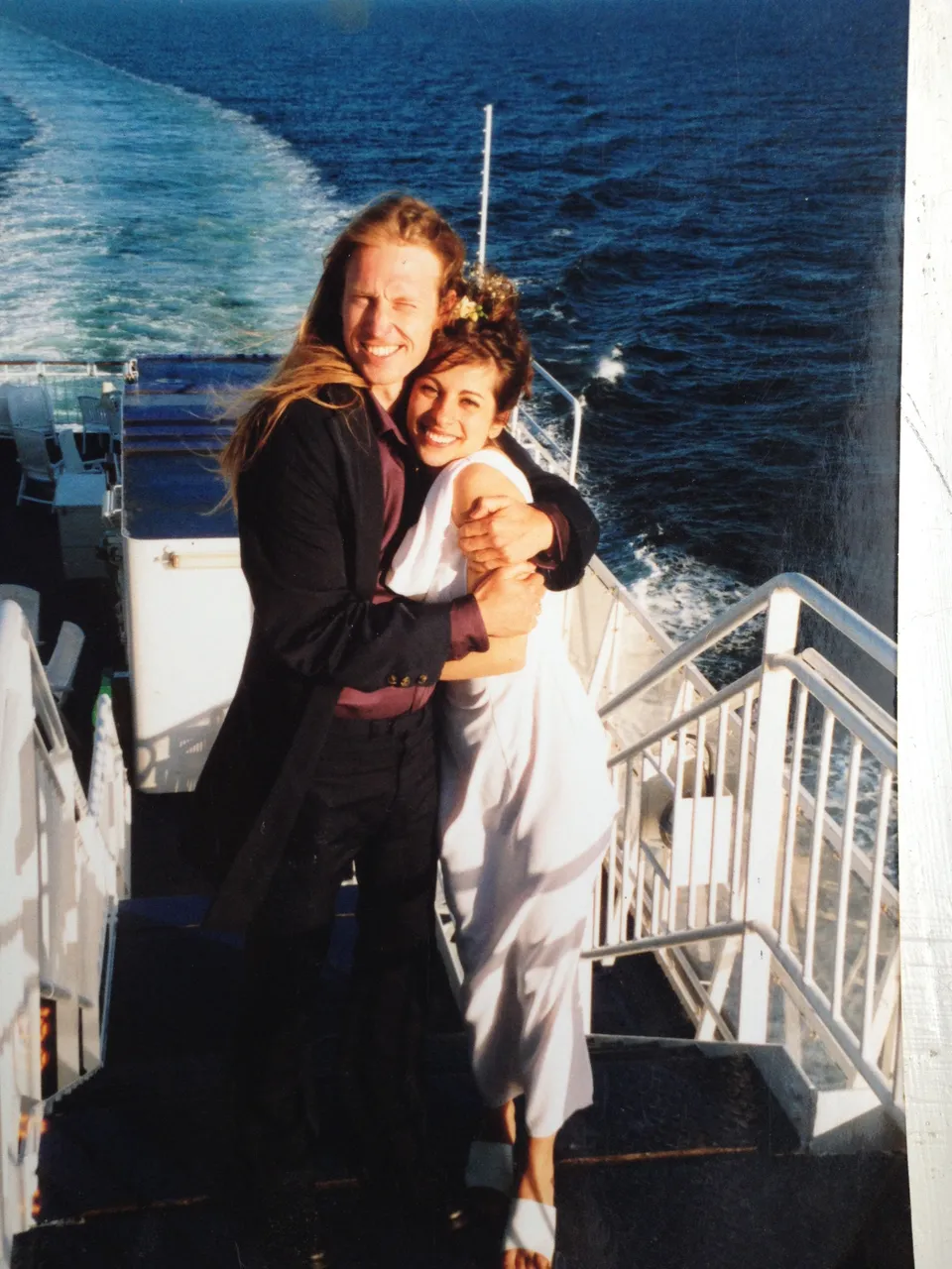 Jacob og Ecaterina Moth som nygifte i 2000, i en tæt omfavnelse på dækket af et skib med havet og kølvandet bag sig. Hun i hvid kjole med blomster i håret.
