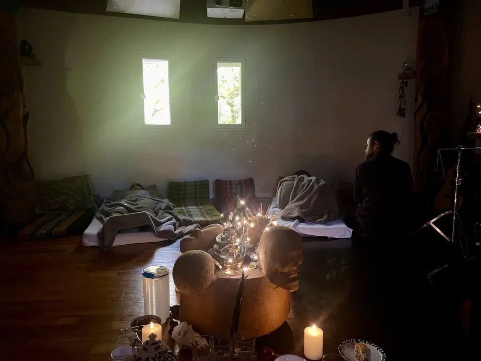 Ayahuasca ceremoni for to i Rundsalen: to mennesker ligger under tæpper på madrasser, alteret med lys står forrest, og en guide sidder og våger over dem
