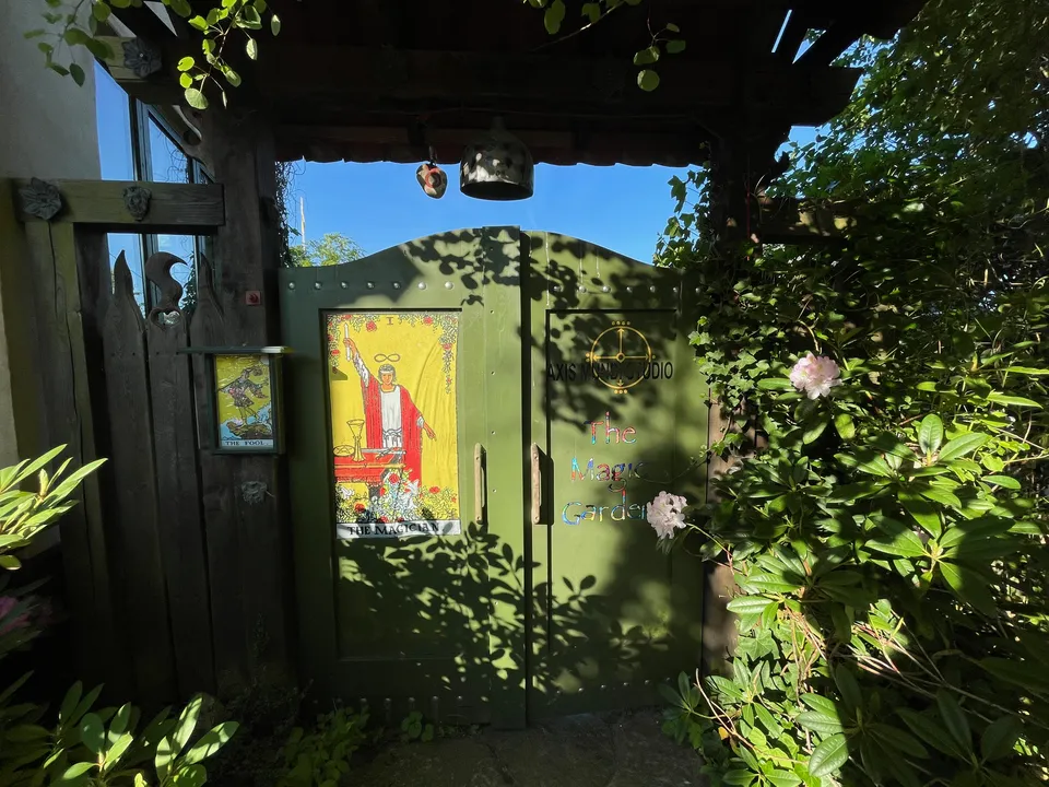 The green garden gate seen from inside on a summer day, with tarot cards on the gate and flowering bushes along the path