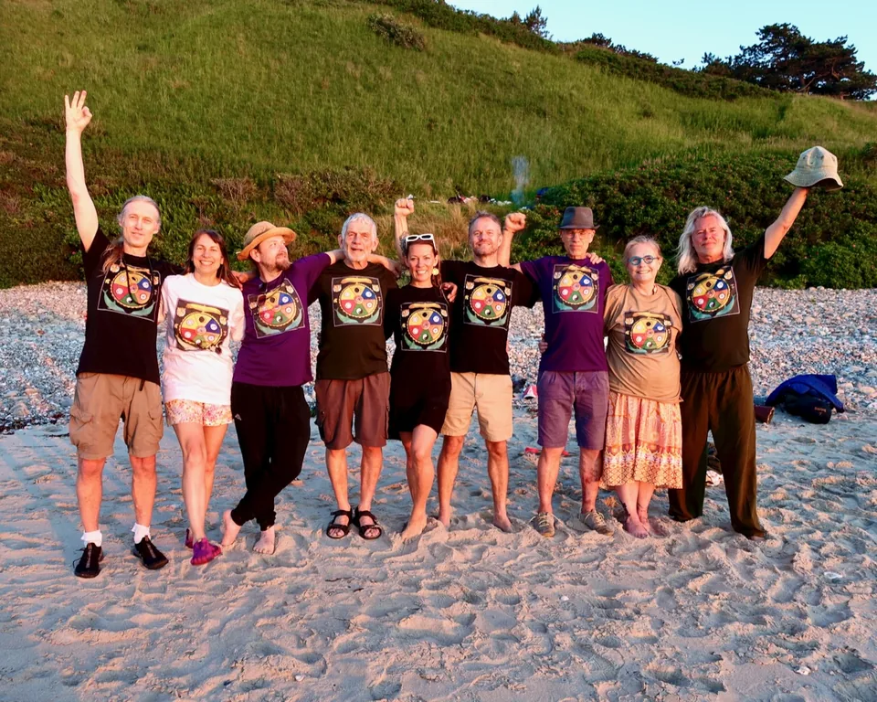 Jacob, Ecaterina og teamet står arm i arm på en strand i aftensol, i ens T-shirts med mandala-tryk, flere med armene i vejret