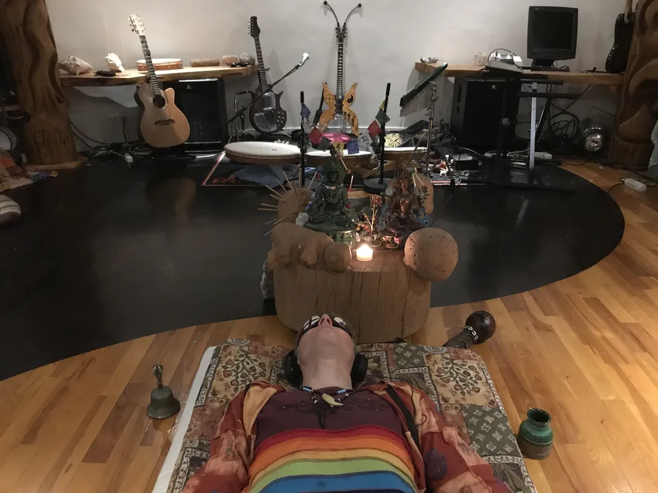 Jacob Moth lying on a blanket in the Roundhall with headphones and an eye mask, in front of a small altar with a candle and the instruments