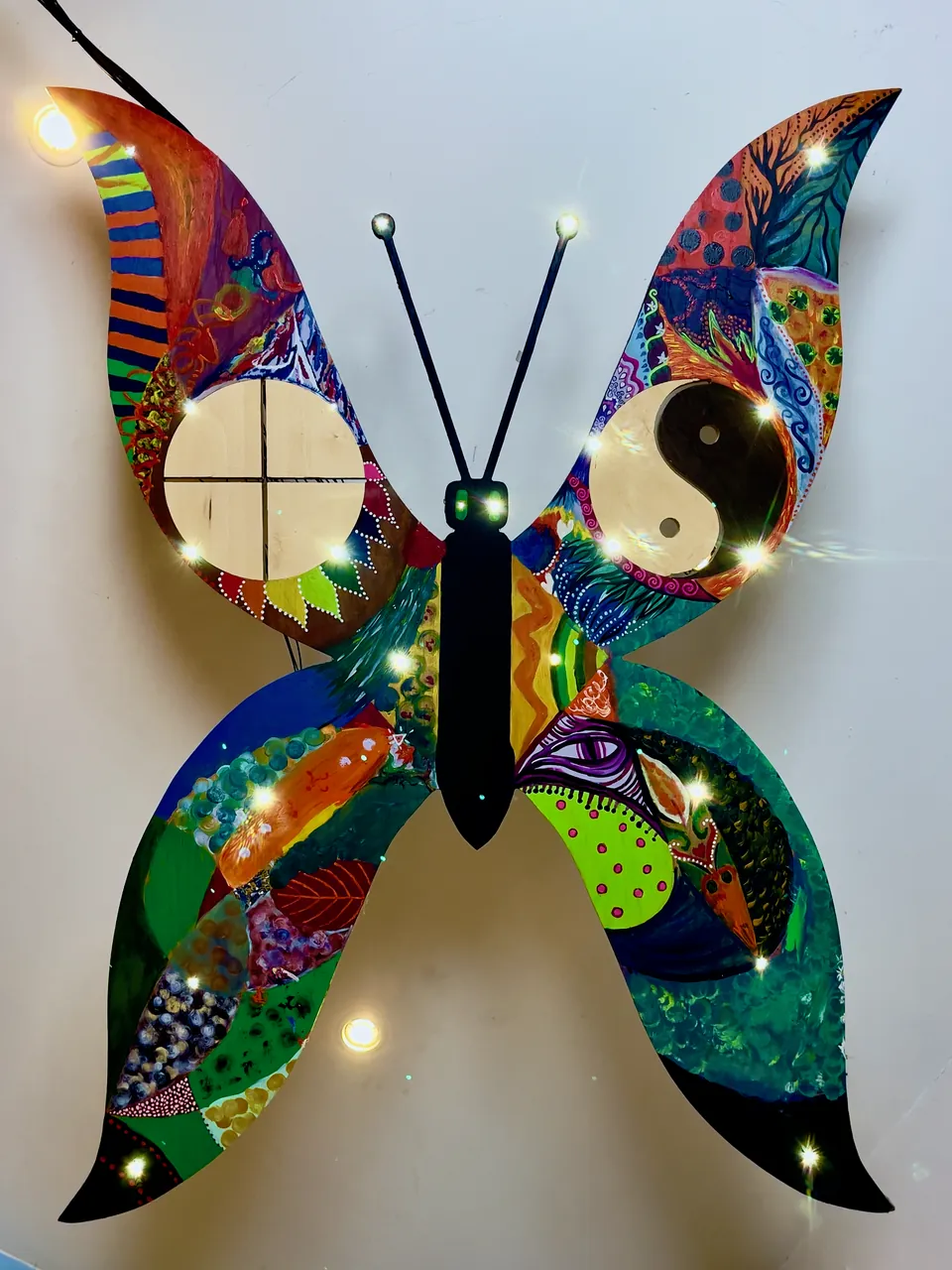 A large painted wooden butterfly with a sun cross and a yin-yang sign on its wings, hovering just below the ceiling in the alcove of the Roundhall