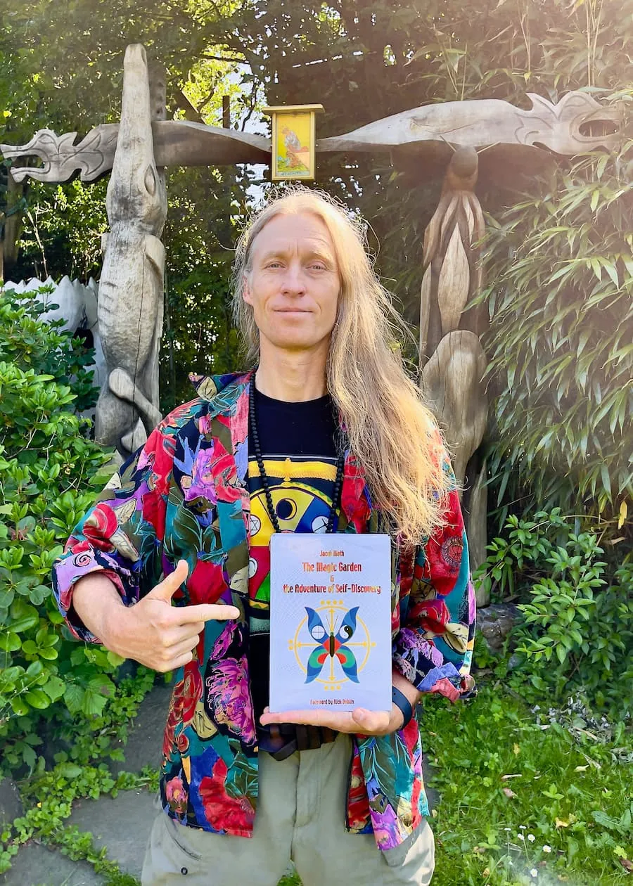 Jacob Moth holds up his new book in front of the wooden portal in The Magic Garden.